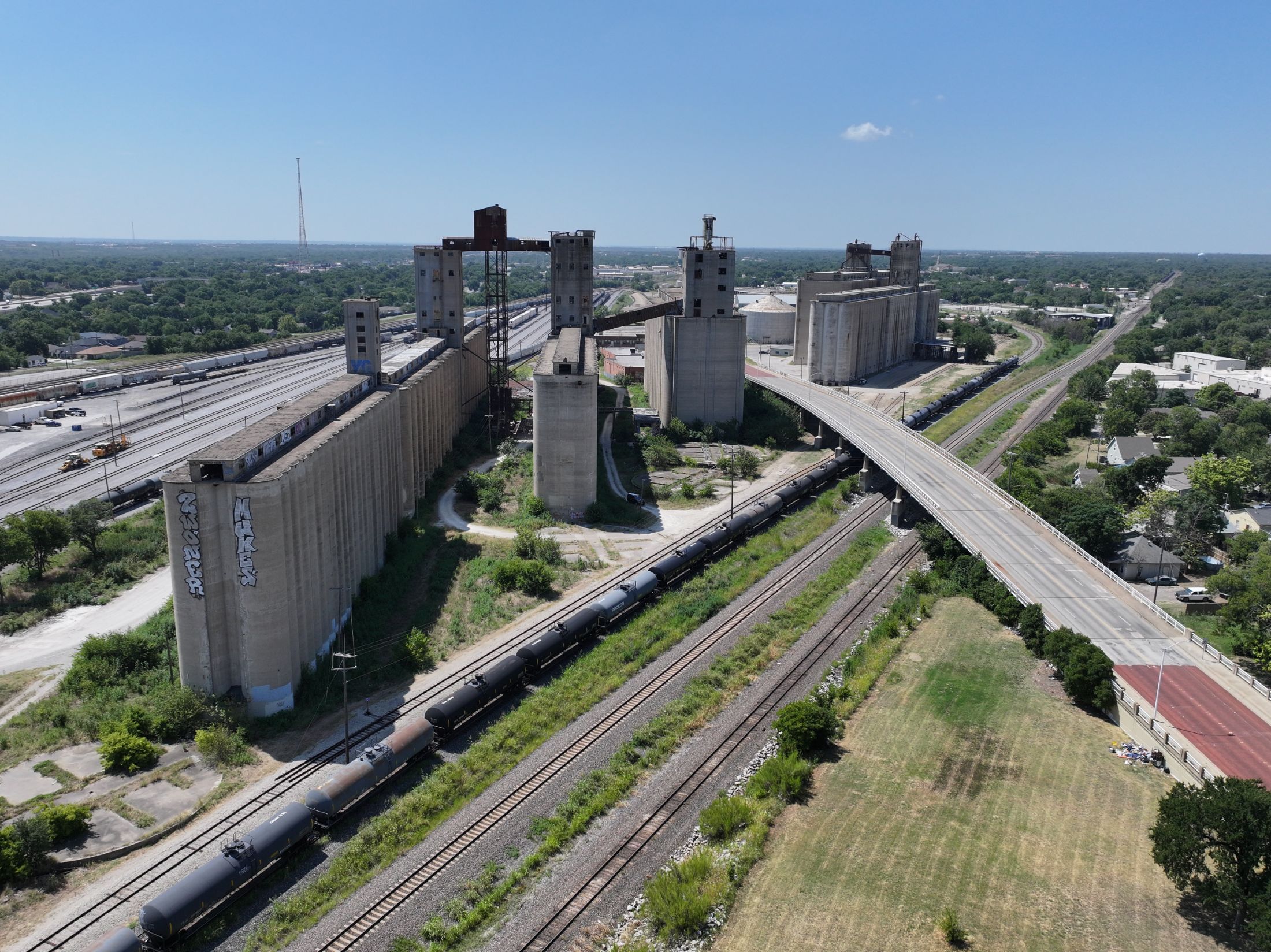 Aerial view of the Main Street Terminal in Fort Worth: a row of concrete storage silos alongside a rail yard, with covered hopper cars on the track and the South Main Street overpass crossing the site.