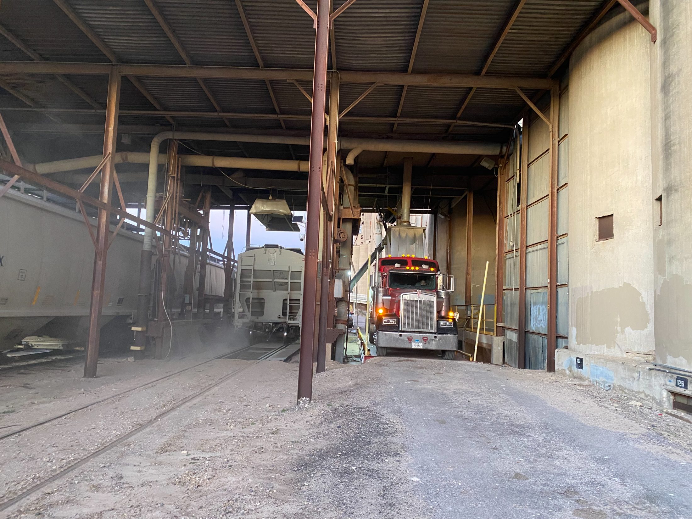 Tractor under the loading spout inside the shed with covered hoppers alongside