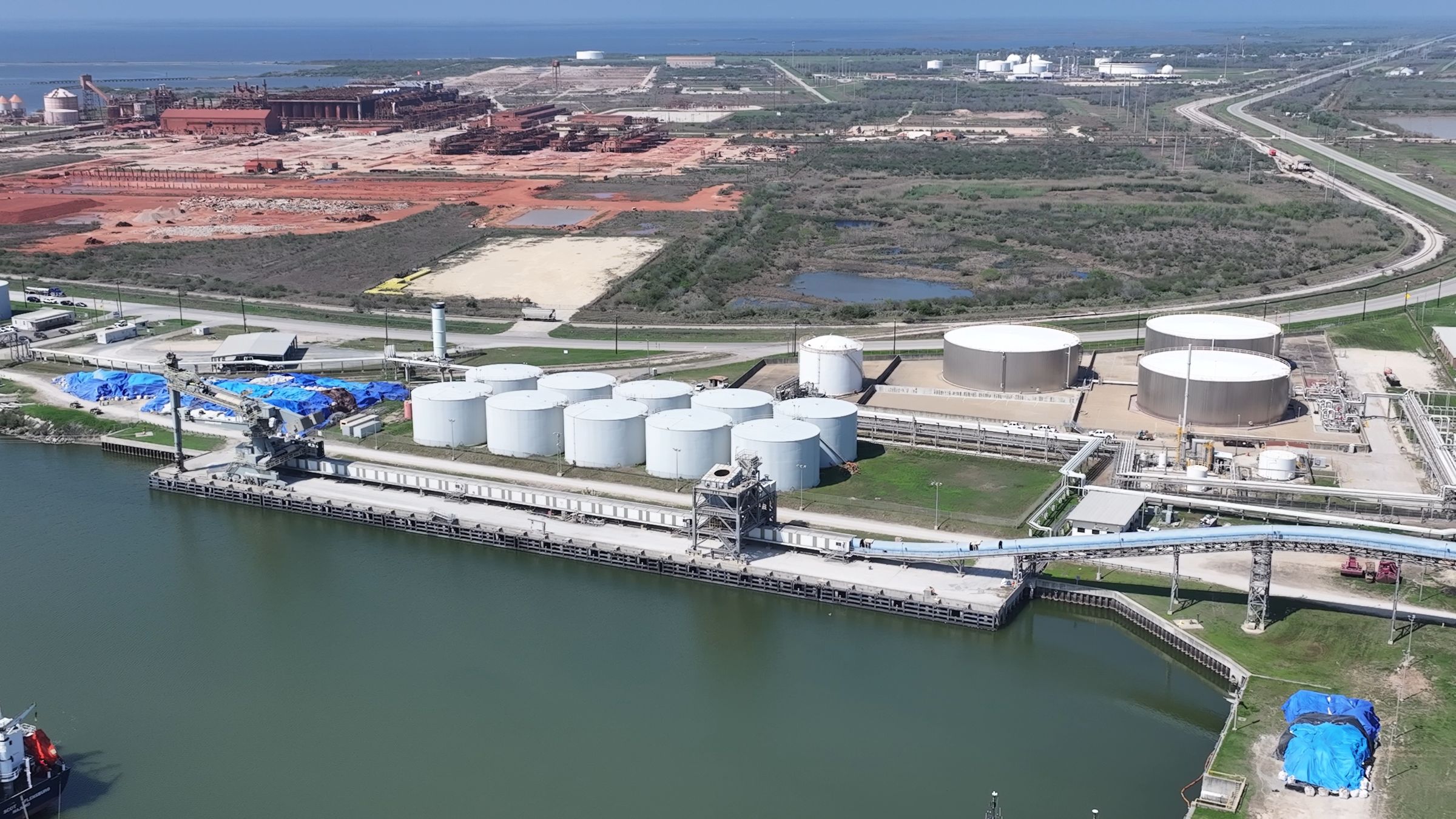 Aerial view of the American Gulf dry bulk dock at Point Comfort, Texas, showing the ship unloader, the covered jetty conveyor along the wharf and the tank farm behind it.